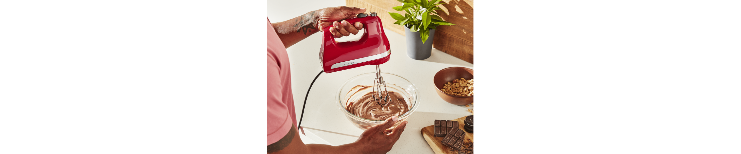 Maker using red KitchenAid® hand mixer to blend chocolate mousse in glass bowl