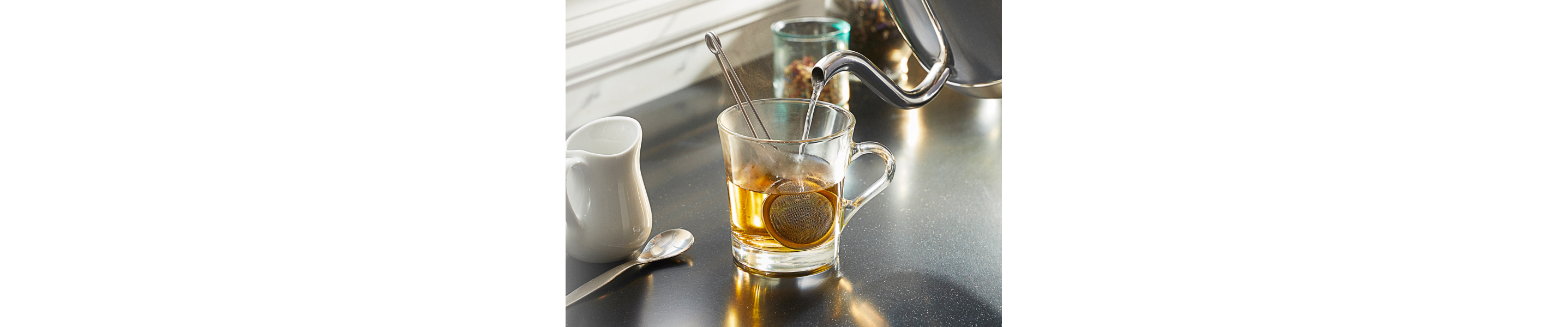 Gooseneck kettle pouring water into a glass mug to steep tea