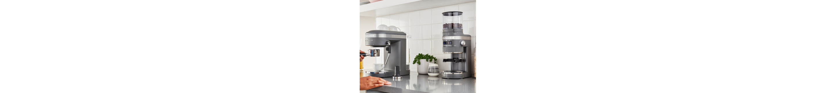 A woman using a KitchenAid® espresso machine next burr coffee grinder in a modern kitchen
