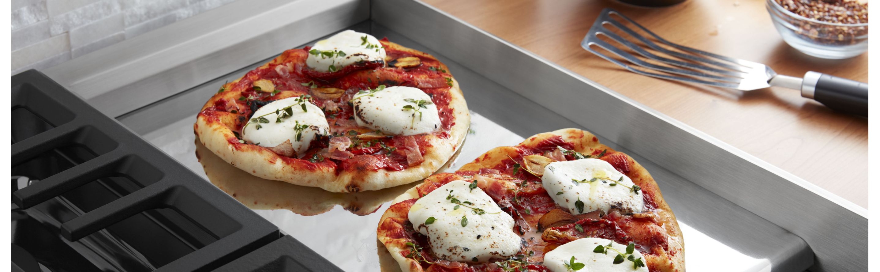 Two homemade Neapolitan pizzas cooking on a chrome electric griddle.