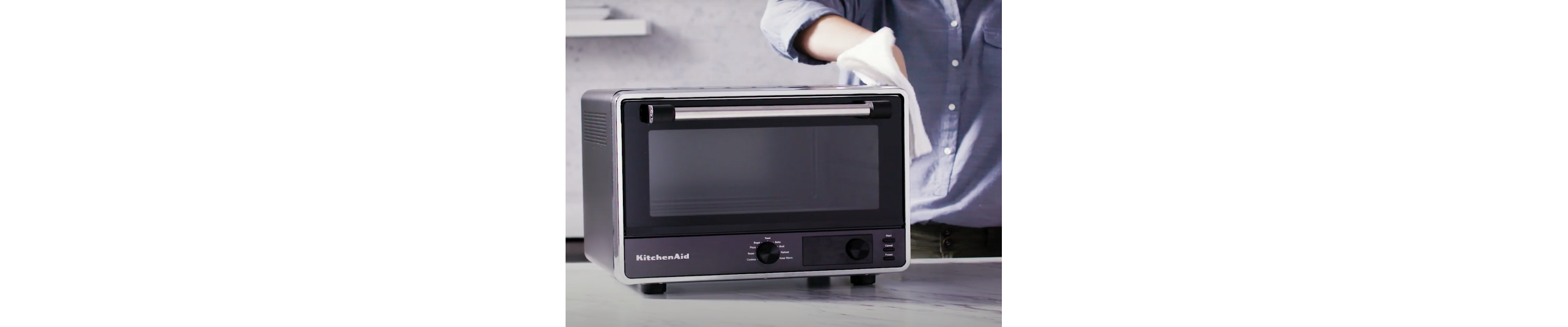 A person cleaning the exterior of a black KitchenAid® air fryer
