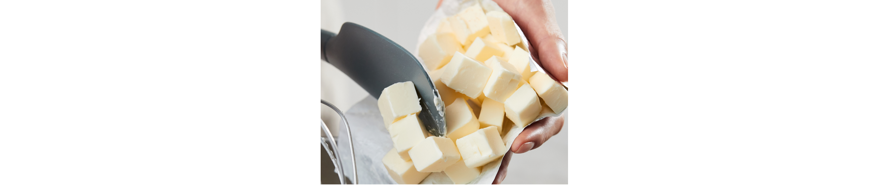 Person spooning cubed butter into a mixer bowl