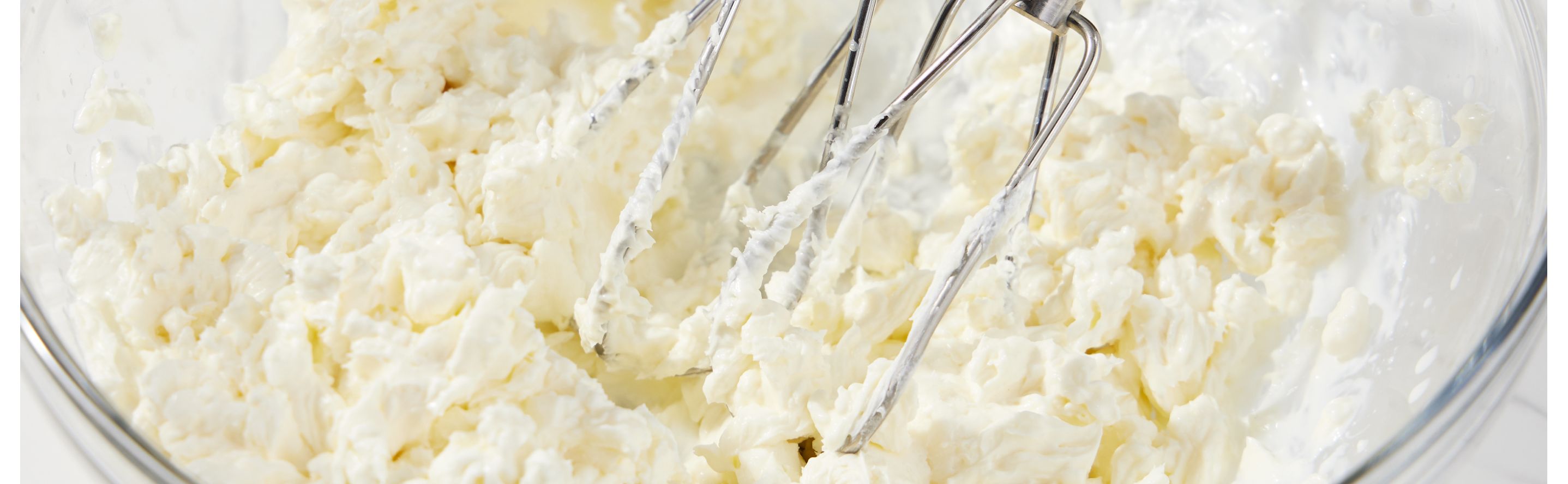 Hand mixer beaters in glass mixing bowl of creamed butter and sugar