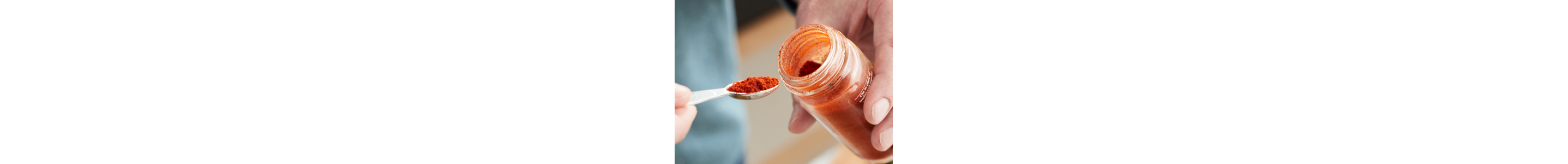 A closeup of hands holding a spoonful of red seasoning and the container.