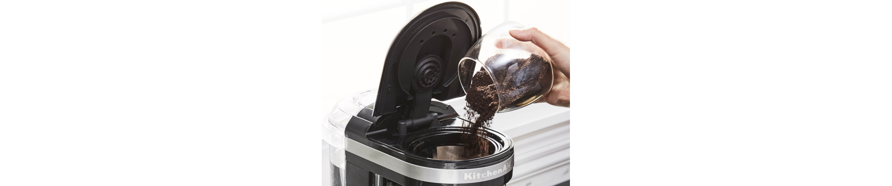 Person pouring coffee grounds into a KitchenAid® coffee maker