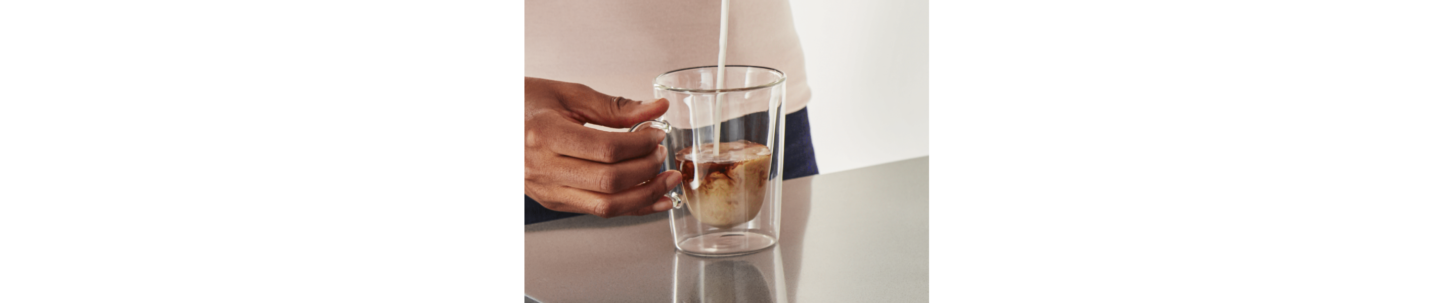 Milk being poured into glass cup of coffee