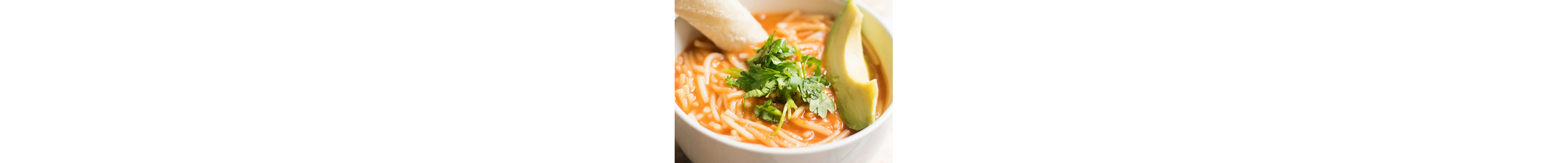 Bowl of sopa de fideo topped with fresh herbs, avocado slices and a breadstick