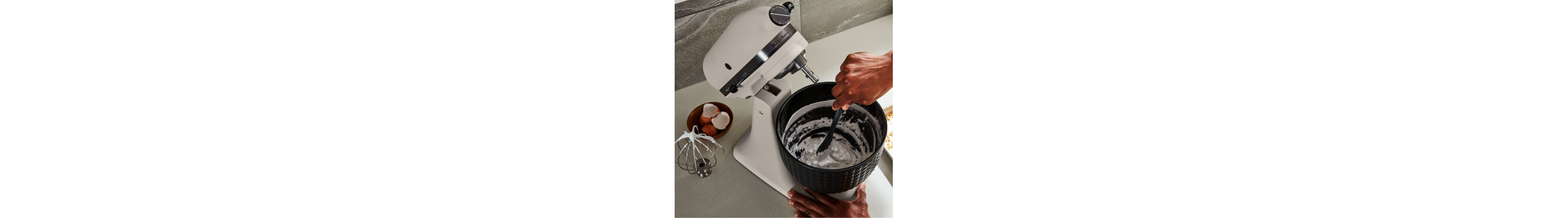 A person removing cream from a white KitchenAid® stand mixer