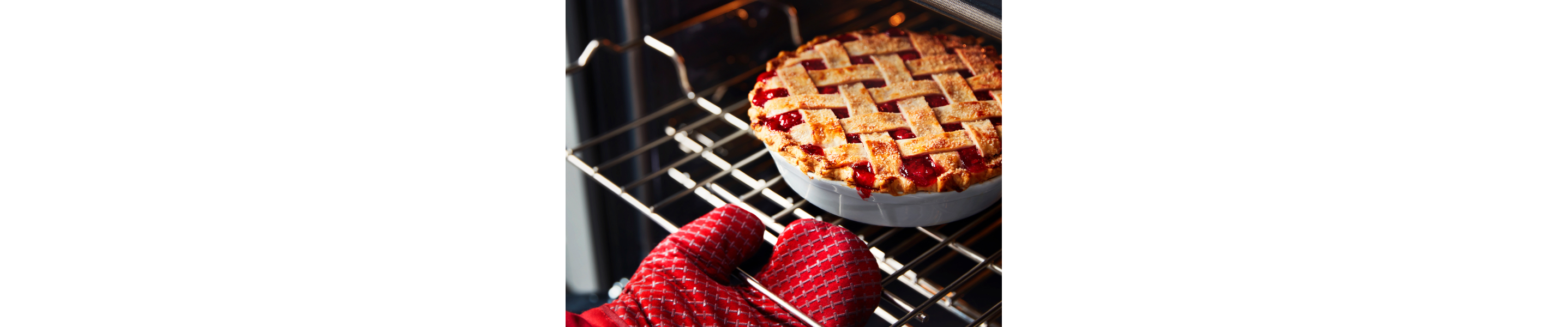 Person with a red oven mitt pulling a cherry pie out of the oven