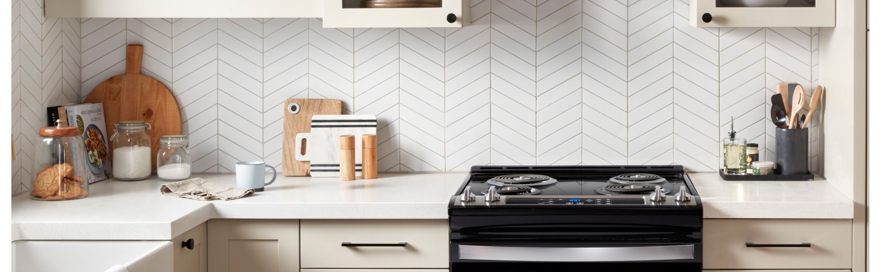 Black electric stove between cream cabinetry in front of a white herringbone backsplash