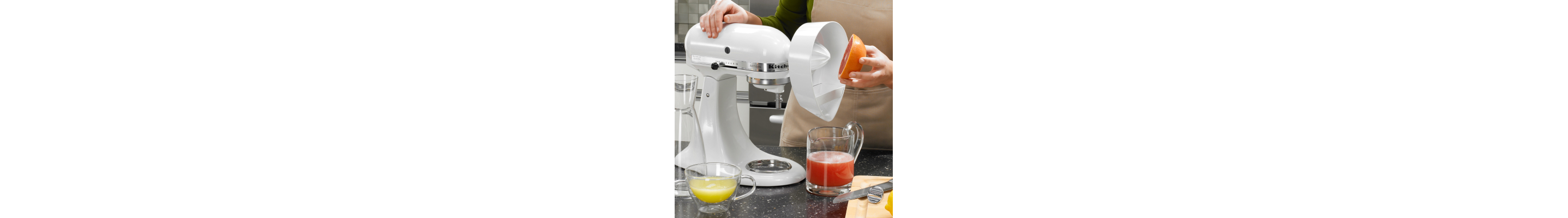 A person using the Citrus Juicer Attachment on a white KitchenAid® stand mixer