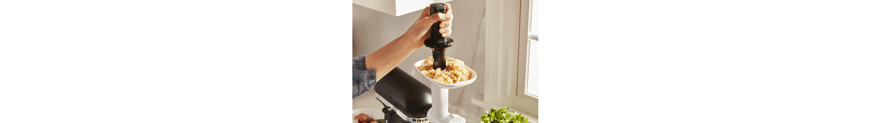 Person using food pusher to feed meat through white food grinder