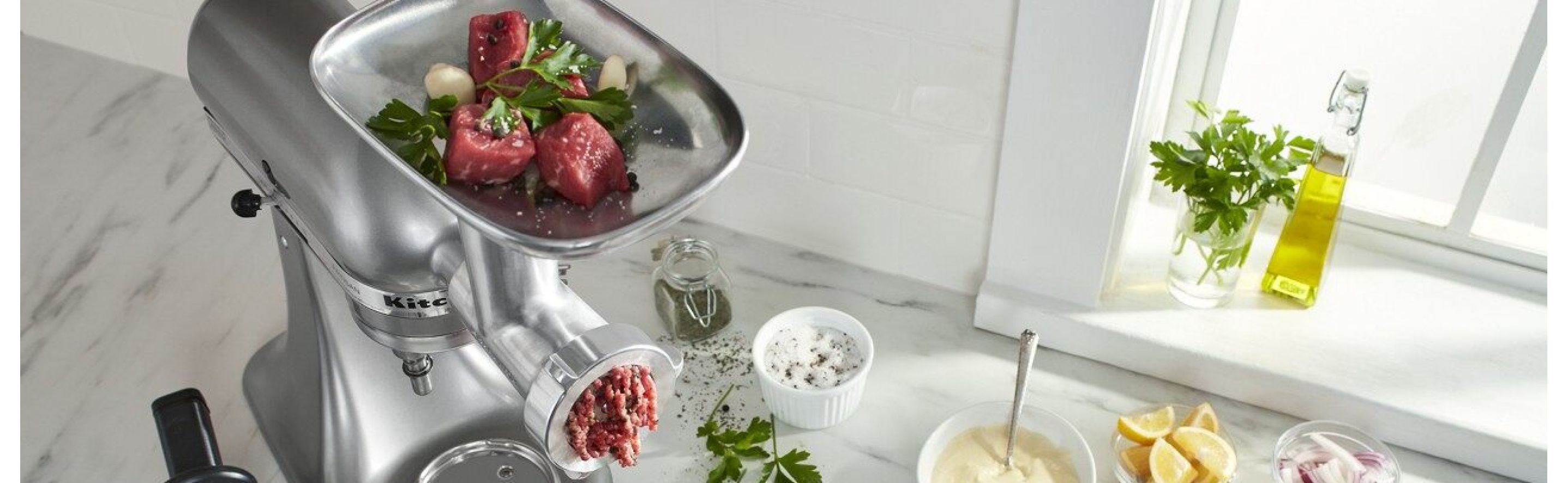 KitchenAid® Stand Mixer with food grinder attachment grinding meat on counter with ingredients