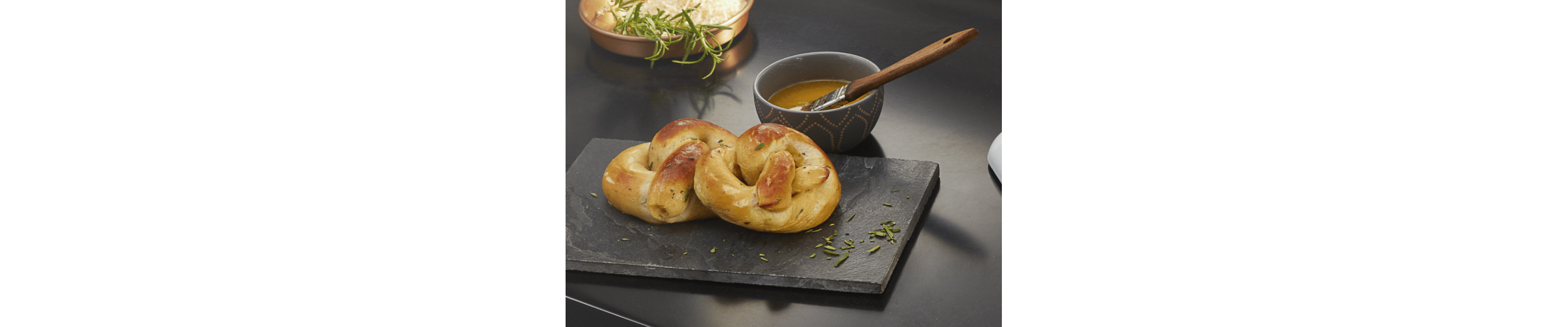 Soft pretzels on a cutting board next to a dish with melted butter and basting brush 