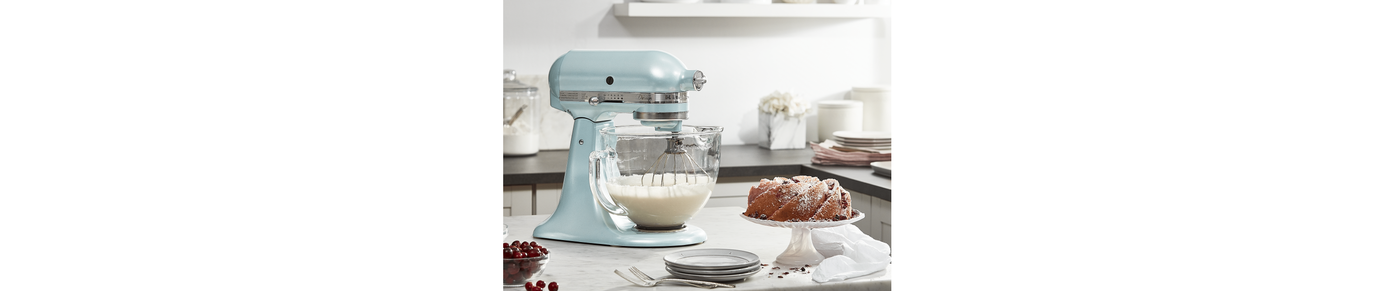 Pearly blue KitchenAid® Stand Mixer with glass bowl whipping cream next to a bundt cake sprinkled with confectioners sugar 