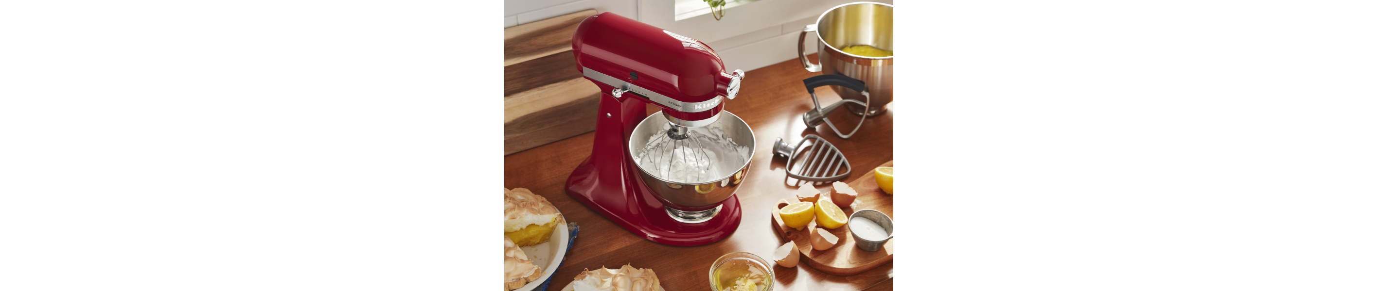 Red KitchenAid® Stand Mixer whipping meringue with lemon meringue pie, lemon curd and lemons on the counter next to the mixer 