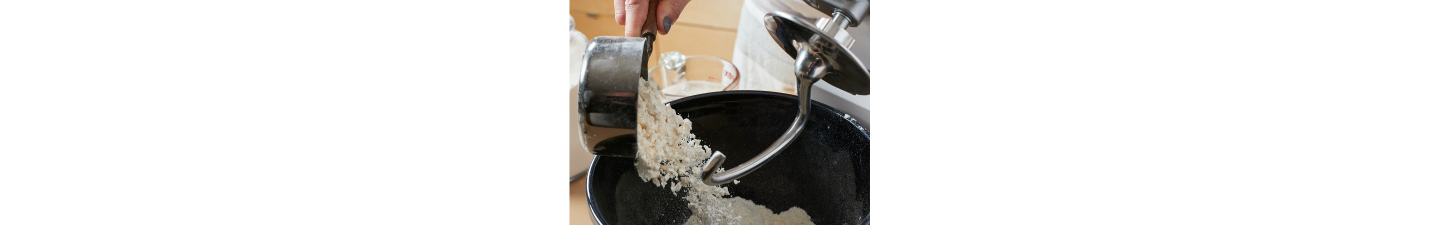 Person pouring flour into a KitchenAid® Stand Mixer with Dough Hook Attachment