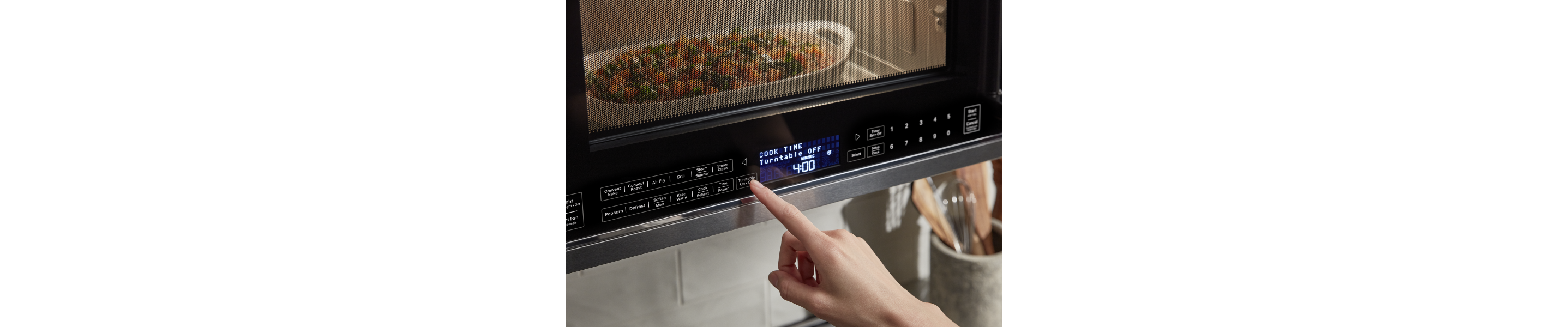 Person selecting settings on an over-the-range microwave steaming a vegetable medley