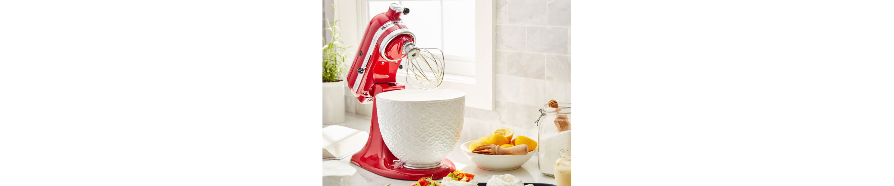 A KitchenAid® stand mixer with a wire whisk/whip accessory on the counter of a modern kitchen.