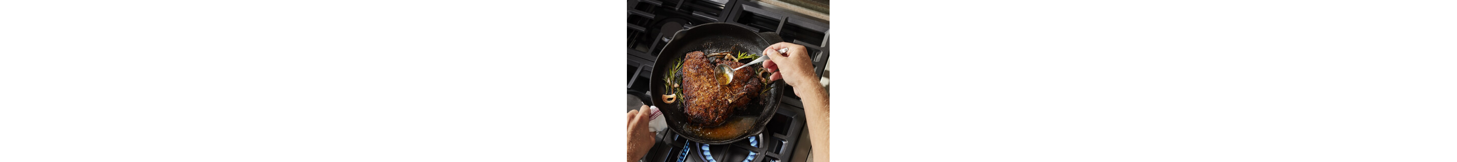 A person basting a steak cooking in a cast-iron skillet