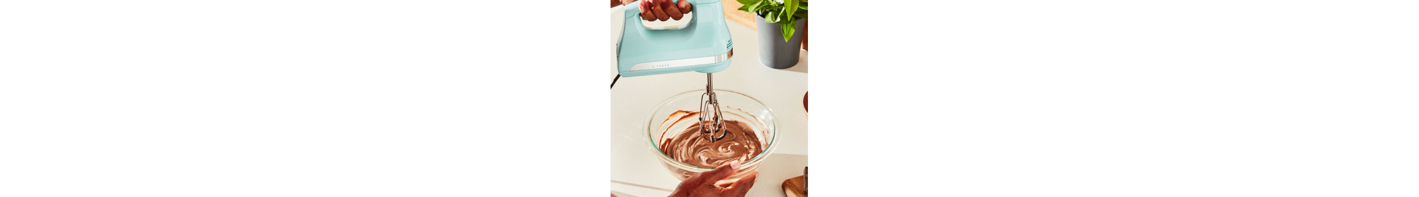 A person mixing chocolate icing with a corded hand mixer