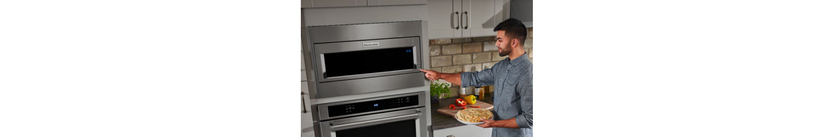 A person holding a plate of food and selecting a button on a KitchenAid® microwave.