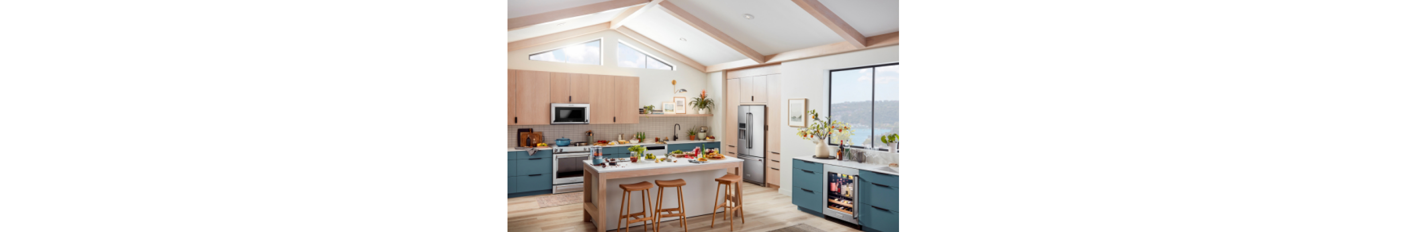An airy, light kitchen with an island and blue-green cabinets and stainless steel appliances.